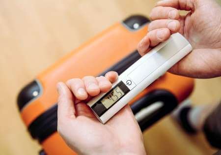 Traveler using a luggage scale to weigh a suitcase
